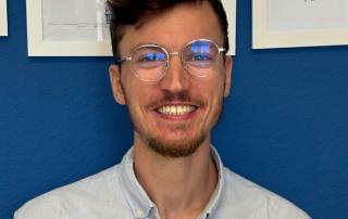 Fotografie einer lachenden Person vor einem blauen Hintergrund